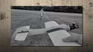 A person in black and white prepares a model airplane for flight, another person stands in the background