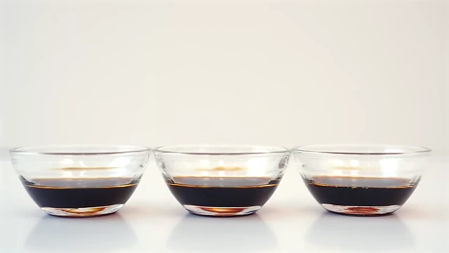 Three small bowls containing different shades of soy sauce, illustrating the distinction between light and dark varieties.