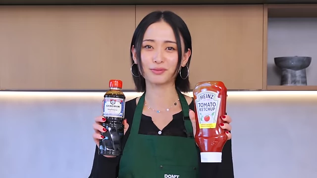 The speaker presenting a bottle of soy sauce and a bottle of ketchup, illustrating the difference between Asian and Western condiments.