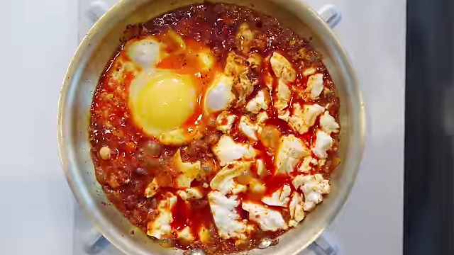 A spicy morning dish with egg and silken tofu simmering in a pan, featuring fish sauce for deep flavor.