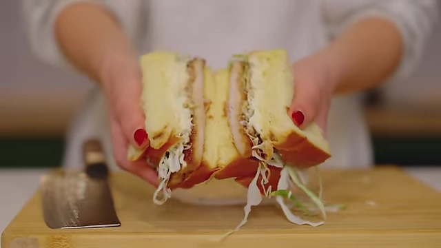A cross-section of a Katsu Sando sandwich, showing the layers of katsu, cabbage, and sauces on brioche bread.
