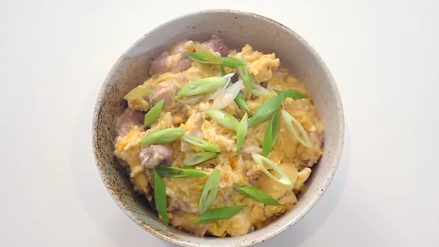 A bowl of Oyakodon, featuring chicken, egg, and onions over rice, garnished with green onions.