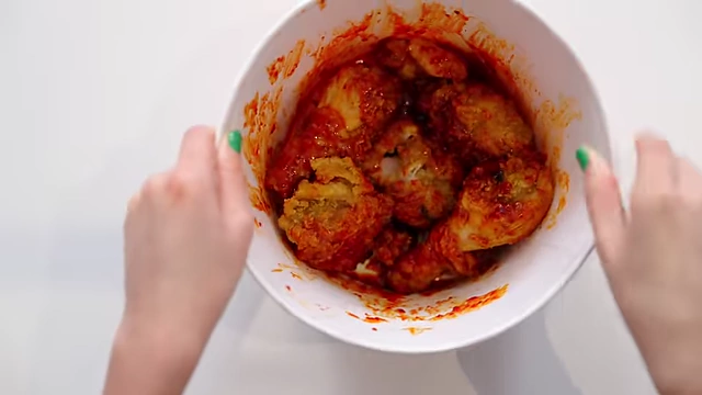 Fried chicken pieces being tossed in a glossy red Yangnyeom sauce.