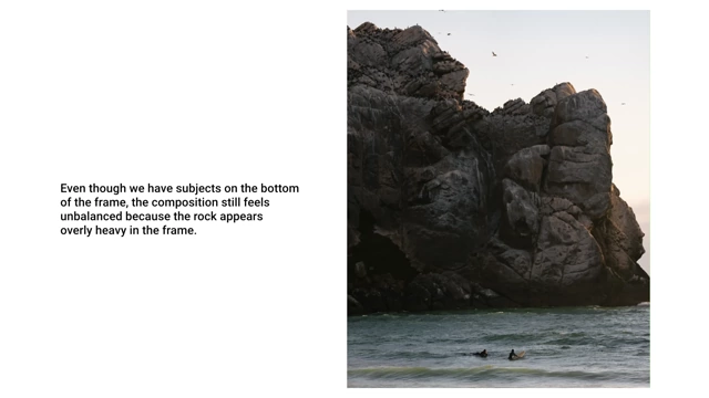 A photo of a large rock formation dominating the frame, making the composition feel unbalanced despite small subjects below.