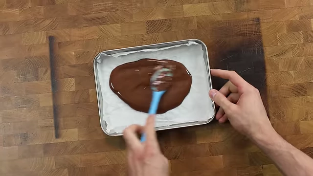 Spreading melted chocolate onto parchment paper for freezing.