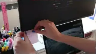 A hand placing a small sticky note on the side of a computer monitor.