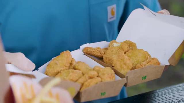 The presenter holding a Chicken McNugget, surrounded by other McDonald's items.