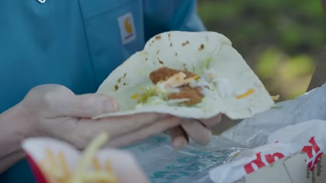 The presenter unwrapping a McDonald's Snack Wrap to reveal fried chicken, sauce, cheese, and lettuce.