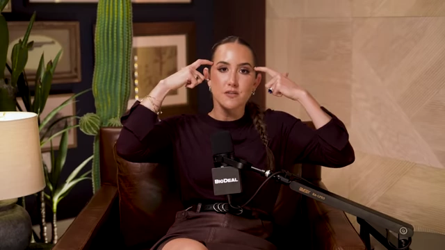 The speaker points to her head, emphasizing that the brain naturally defaults to upward comparison.