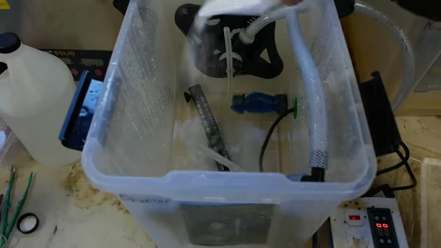 A hand pouring sodium carbonate into the developer tub, demonstrating the preparation of the photoresist developer solution.