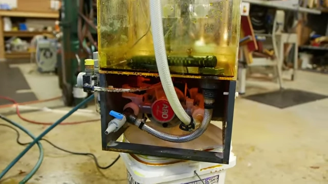 The air-powered pump setup located beneath the etching tank, crucial for generating the high pressure and flow rate needed for effective spray etching.