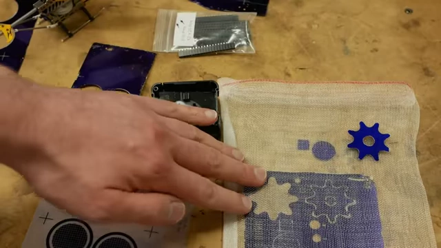 A mesh bag containing a metal panel with etched parts, demonstrating the concept of parts falling free during the etching process.
