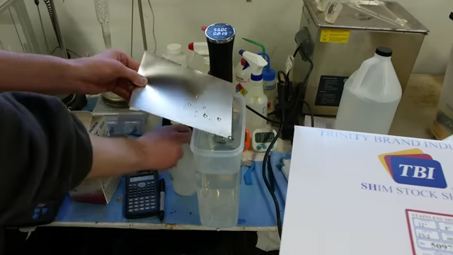 A water break test on a metal sheet, with water beading up, indicating surface contamination before cleaning.