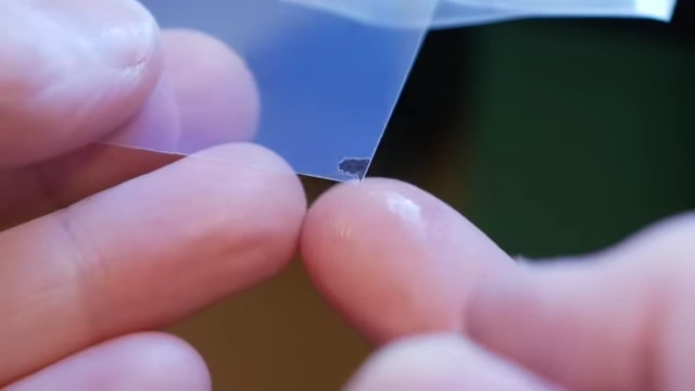 A finger demonstrating the emulsion side of a transparency film, which is designed to absorb and hold inkjet ink for high-contrast masks.