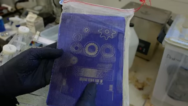 A metal panel inside a mesh bag after photoresist development, showing the revealed pattern and good registration.