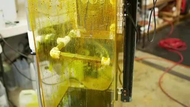 A close-up view inside the etching machine, showing the high-pressure spray of etchant actively dissolving the exposed metal, accelerating the process.