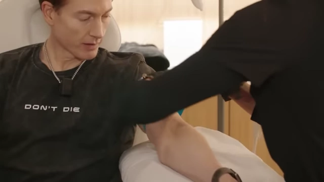 Bryan Johnson wearing a 'Don't Die' shirt while undergoing a blood draw, symbolizing his regimen