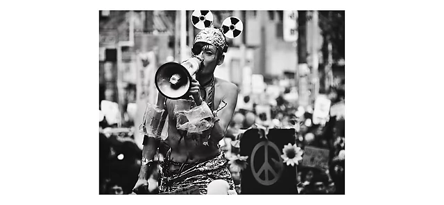 A woman with a megaphone and radiation symbol ears in a striking street protest scene