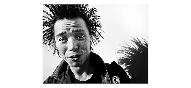 A man with spiky hair and a punk rock aesthetic looks intently at the camera
