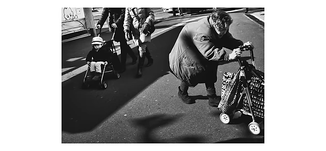 An elderly woman pushing a shopping cart alongside a child in a stroller on a Tokyo street