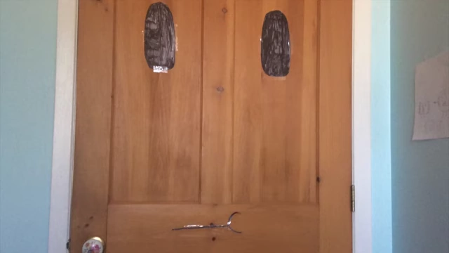A plain wooden door with two black eye shapes and a line for a mouth.