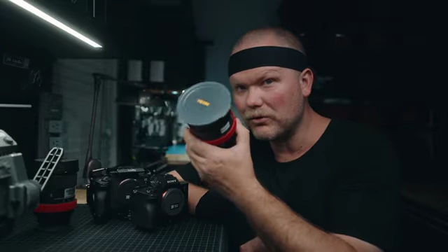 The speaker displays a zoom lens, recommending versatile 24-105mm and 24-70mm lenses for interviews and B-roll.