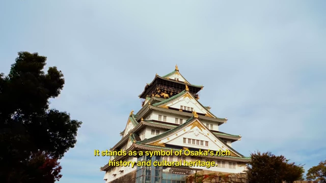 The majestic Osaka Castle, a multi-story pagoda-style structure with green roofs and golden accents, stands proudly against a blue sky, symbolizing the city's rich history.