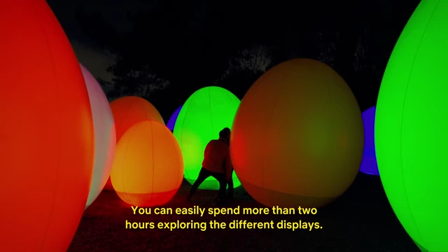 Visitors walking among large, glowing orb installations that change colors in the TeamLab Botanical Garden at night.