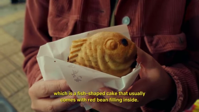 A hand holding a warm taiyaki (fish-shaped cake) with red bean filling, a popular Japanese street snack.