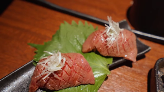 Two pieces of perfectly grilled yakiniku nigiri, served with thinly sliced green onions on a shiso leaf.