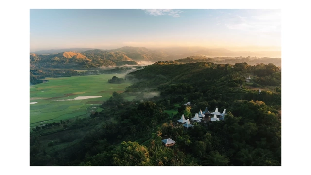 An aerial view of a lush green valley with traditional houses and mountains in the distance during golden hour