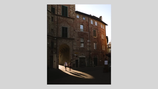 Two people walking into a sunlit alleyway, casting long shadows, in a quiet European town during sunrise