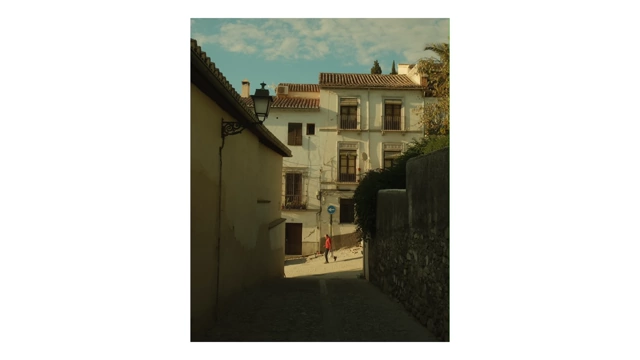A sun-drenched street in a Spanish town, with a person walking a dog in the distance