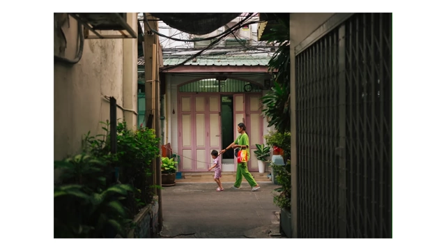 A mother and child walking down a narrow, plant-lined alleyway in Bangkok, capturing a moment of local life