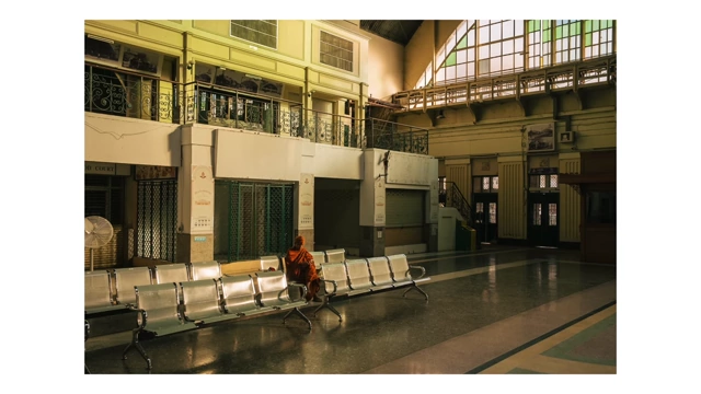 A monk sitting alone on a bench in a quiet train station hall, emphasizing solitude and light