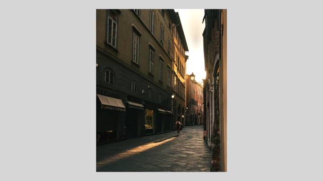 A person cycling through a quiet, sunlit European alleyway during sunrise