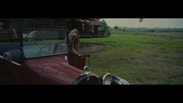 A character arriving in a vintage car at a rural setting in the film's opening scene.