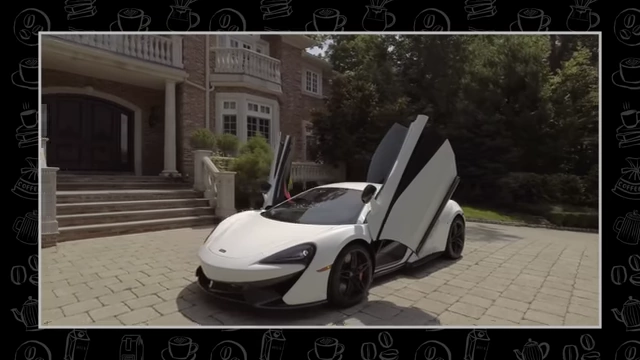 A white McLaren sports car with its distinctive dihedral doors open, parked in a driveway.