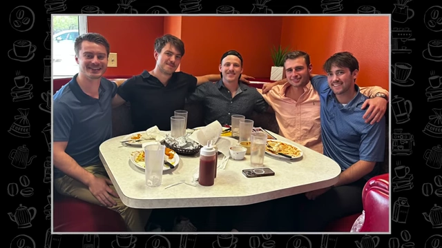 A group of five young men smiling and posing for a photo around a dining table in a restaurant.