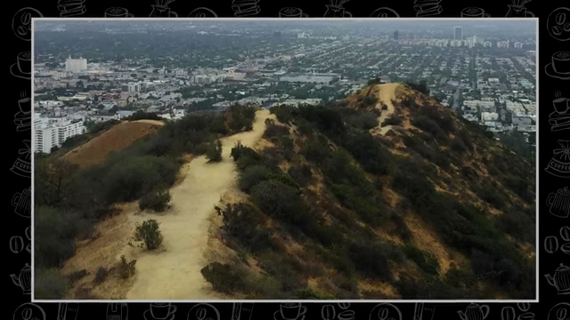 A hiking trail winds through hills with a city skyline in the background.