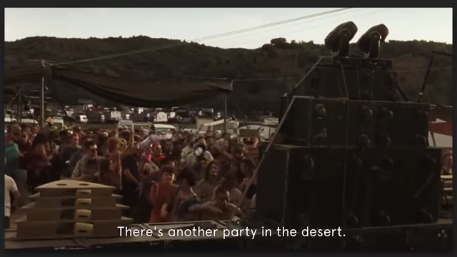 A large outdoor rave in a desert setting with people dancing and massive speakers in "Sarat."