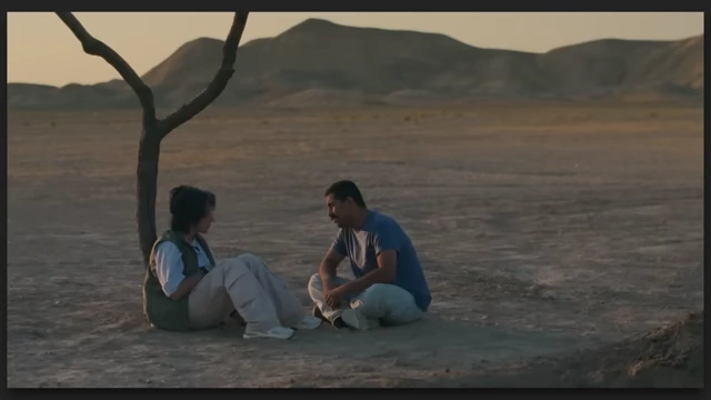 A man and a woman sitting on the ground next to a small tree in a vast desert from "It was Just an Accident."