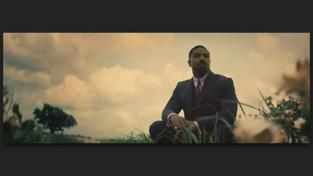 A man in a suit crouching in a grassy field with a cloudy sky in "Sinners."