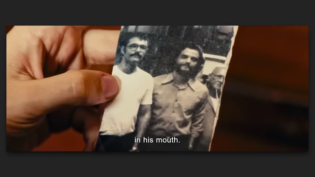 A hand holding a torn black and white photograph of two men in "The Secret Agent," symbolizing memory and disappeared persons.