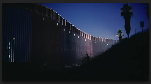 A tall, illuminated border wall at night, symbolizing the "dying world" and societal divisions in "One Battle After Another."