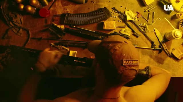 A soldier in uniform cleaning a rifle, with a 'BAKHMUT' cap visible