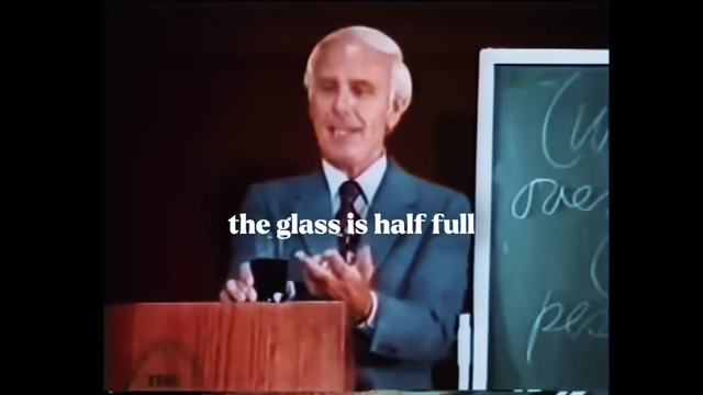 Jim Rohn holding a glass, illustrating the "glass half full" perspective of an optimist.