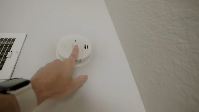 A hand presses the test button on a smoke alarm.