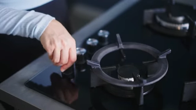 A hand turning on a gas stove burner.