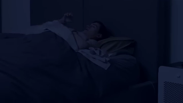 A person sleeping with a portable air purifier visible in the bedroom.